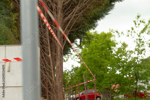 Red and white tape marking event boundary near trees and parked van blurred tape lines create sense of organized restriction and anticipatory atmosphere