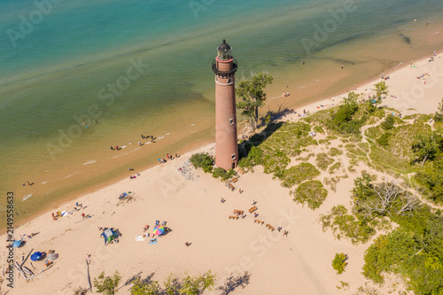 Aerial view of Little Sable Point Lighthouse standing on a sandy beach along the shore of Lake Michigan with people relaxing on the sand in Mears, Michigan, United States.