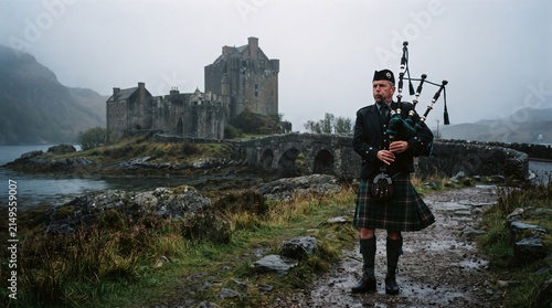 Scottish highlander standing near eilean donan castle in foggy weather