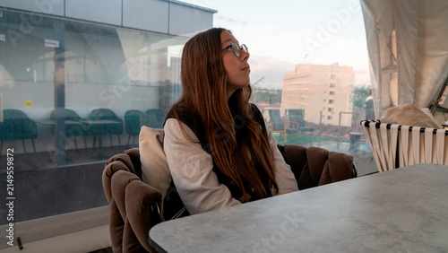 Obraz na plátně Young woman sitting at a table in a cafe with a view of a city at sunset The Sky cafe at the Tsum supermarket in Grodno, Belarus, on the pedestrian old Lenin Street on July 15, 2026