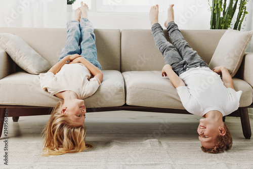 Foto Two happy children lie upside down on a beige sofa in a bright living room