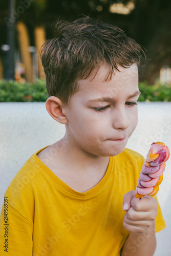 Little boy in a yellow shirt enjoying a colorful ice cream popsicle outdoors, savoring a sweet summer treat with a joyful expression