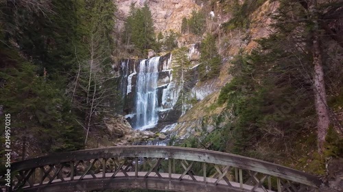 Vue aérienne en drone de la grande cascade du cirque de Saint Même, au cœur du massif de la Chartreuse, entourée d’une forêt de montagne. Un pont en bois traverse le cours d’eau en contrebas de la cas