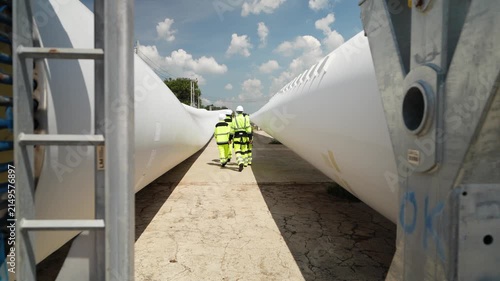Workers walk between wind turbine blades at a construction site in sunny weather