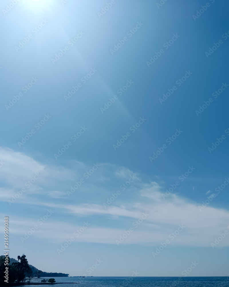 Obraz premium Blue ocean and sky meet at a distant horizon, with soft clouds and a small coastal landform creating a calm vertical composition. Ideal to decorate phone screens, wellness content, mobile background. 