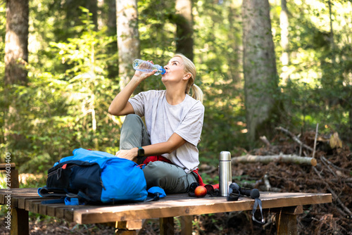 Принти на полотні Woman hydrating with water from a bottle while sitting on a wooden bench during