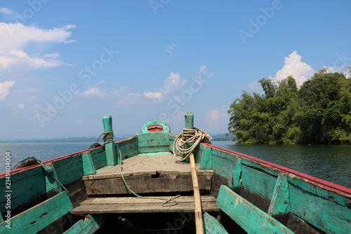 Fotografie Weathered green wooden boat floating calmly on clear blue water during a bright