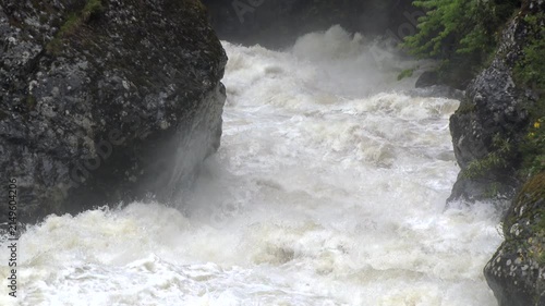 Super slow motion flood river surges through a mountain stream with raging white water and foam.