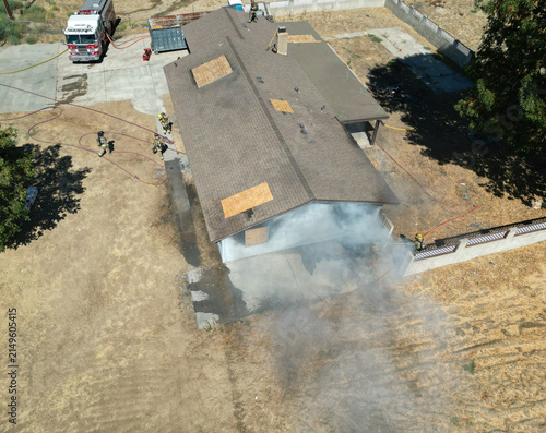 Firemen and women practicing to put out fires on an abandoned house looking at from a UAV Drone as smoke billows from the windows and roof so Fire Fighters can practice their skills