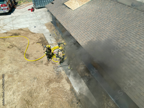 Firemen and women practicing to put out fires on an abandoned house looking at fire fighters preparing to enter a practice building with their equipment to rescue people inside and put out the fire.