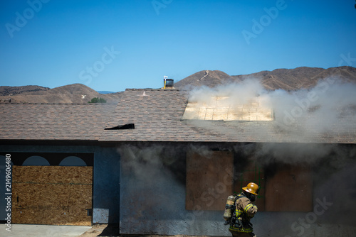 Firemen and women practicing to put out fires on an abandoned house looking at fire fighters preparing to enter a practice building with their equipment to rescue people inside and put out the fire.
