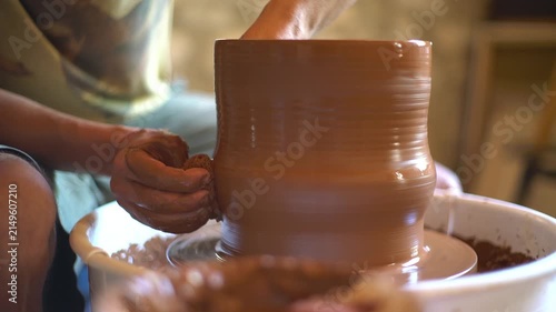 A ceramics artist shapes wet clay on a spinning pottery wheel in a studio.