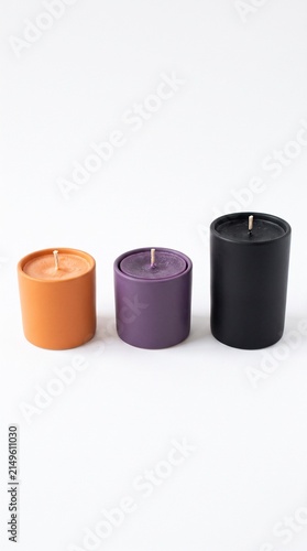 Three Halloween themed candles in orange purple and black colors on a white background for seasonal decor