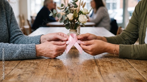 Two women holding a pink ribbon together symbolizing breast cancer awareness and support during October