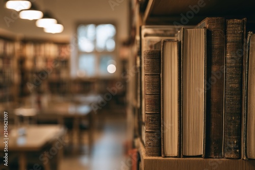 Close-up of vintage books on a shelf in a library, with blurred tables and lights beyond