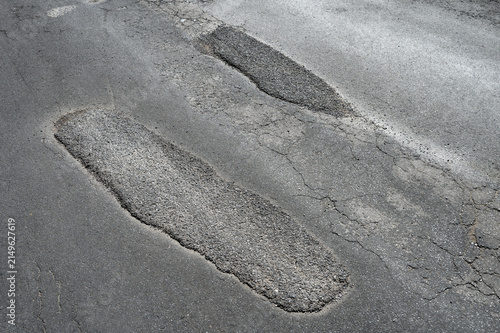 Foto Close-up of a damaged asphalt road surface featuring rough patched potholes, cracks, and uneven pavement in bright daylight