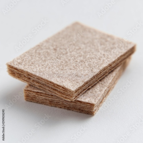 A small stack of rectangular, fibrous brown felt pads or material swatches isolated on a clean white background.