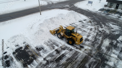 Aerial view of a yellow wheel loader clearing snow from a parking lot in winter