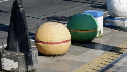 Colorful round concrete spherical bollards in yellow and green installed along an urban city sidewalk.
