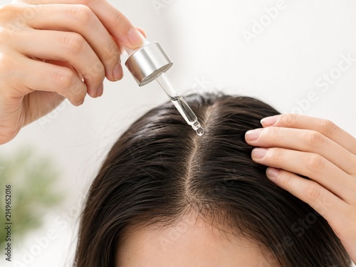 Cuadro en lienzo Person applying hair serum or scalp treatment with a dropper to their hair parti