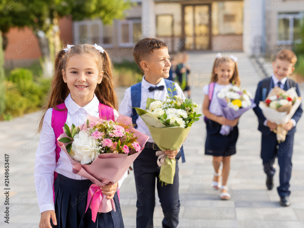 Fototapeta premium Happy Schoolchildren with Flowers and Backpacks on First Day of School