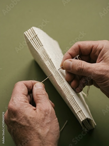 Hands stitching the spine of a handmade book, bookbinding craft