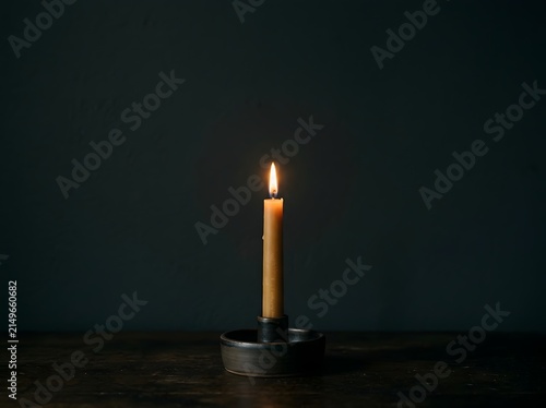 Single lit candle glowing in dark room, hope concept
