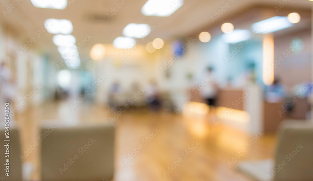 Obraz premium Blurred image of a modern hospital reception area with soft lighting, featuring waiting chairs and people in the background, creating a calm atmosphere.