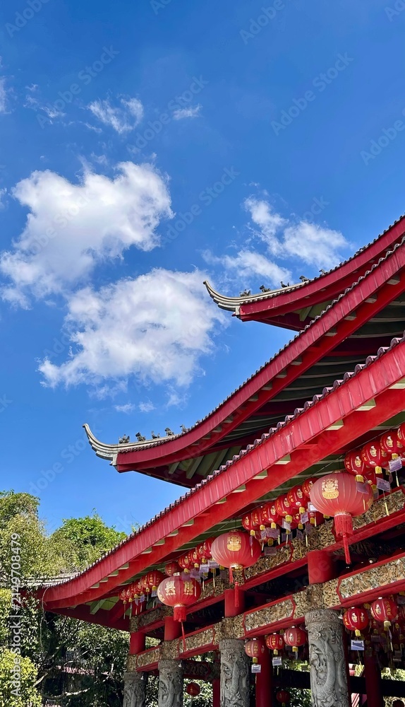 Obraz premium Low angle view of a magnificent multi tiered red Chinese temple building with traditional carved pillars against a vibrant blue sky.