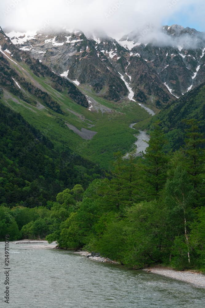 Obraz premium Mountain valley river forest snow cloud alpine landscape snow capped mountain valley with green forest and river under low cloud in remote alpine wilderness, natural travel scenery