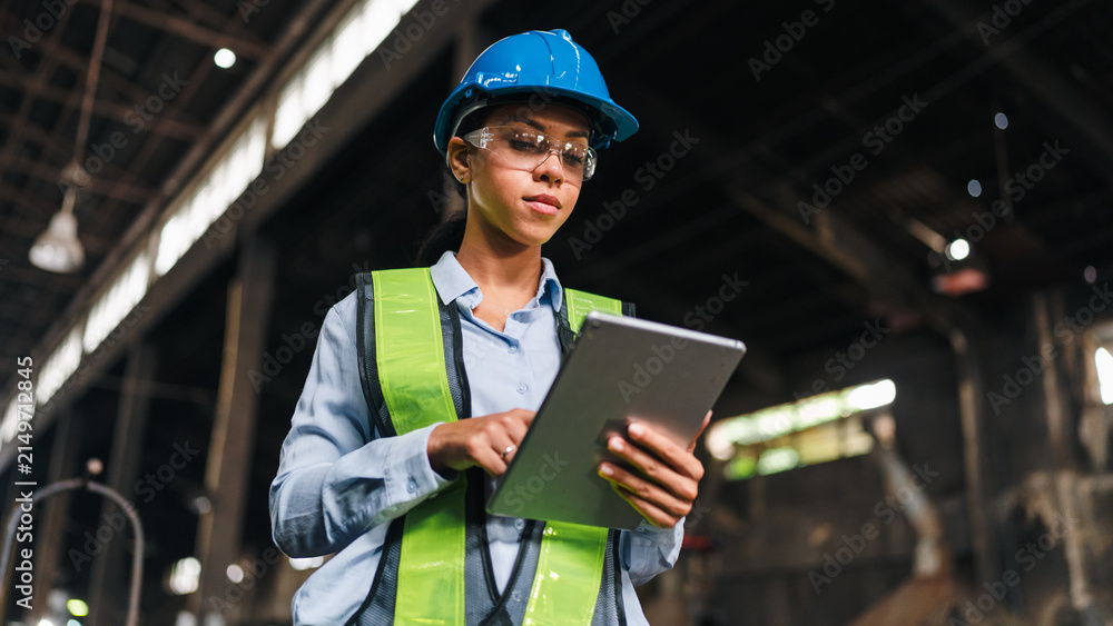 Fototapeta premium Engineer worker safety helmet tablet factory woman vest inspection focused female engineer using tablet in industrial factory, wearing safety gear during work