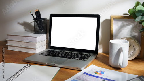 Home office desk with a laptop blank screen, notebook, calculator, financial documents, coffee mug, books, and green plant.