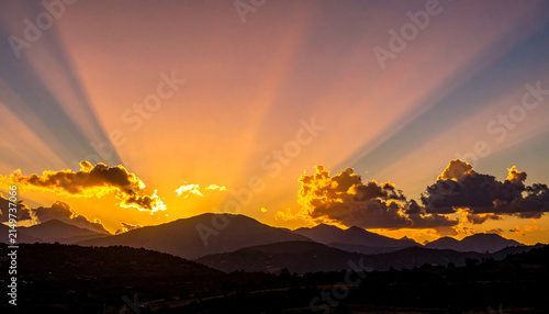 Vibrant sunset over mountain peaks with radiating sunbeams and clouds 1
