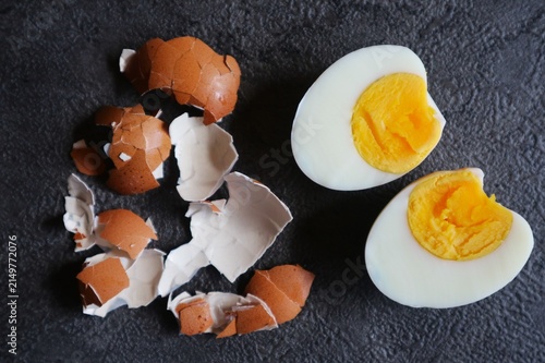 Foto This photo shows a hard-boiled egg cut in half, surrounded by the brown eggshells that have been peeled off