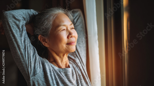 Calm elderly woman taking a peaceful moment to reflect by the window bathed in gentle natural light