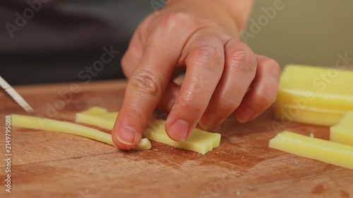 Woman hand slicing cheese with kitchen knife on wooden cutting board