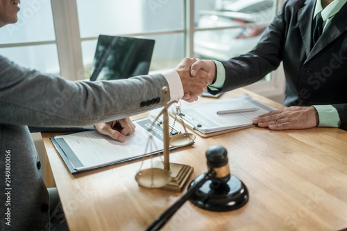 Business people shaking hands across a desk after a legal agreement in an office with documents, gavel and scales of justice