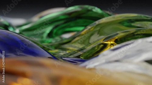 Glass art waves flow in vibrant blue green and amber hues across a smooth glossy sculpture surface creating dynamic abstract reflections and fluid motion in a macro studio lighting setup