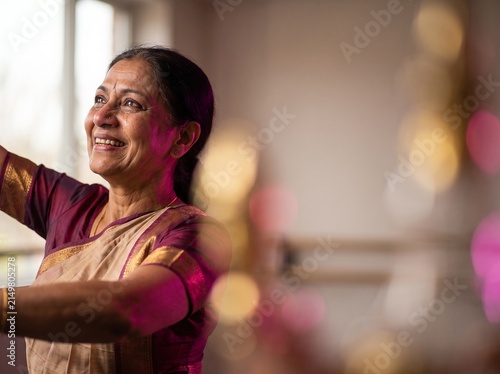 Portrait of happy mature Indian woman in traditional saree dancing in sunlit room