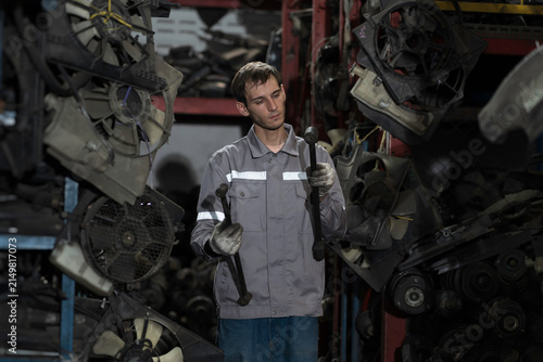 Automotive spare parts warehouse. Male warehouse worker inspecting spare parts in old auto parts warehouse. Male mechanic worker checking spare parts in workplace