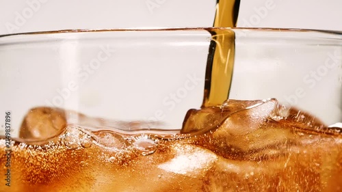 Slow motion closeup pouring cola with ice cubes and bubbles, soft drink texture