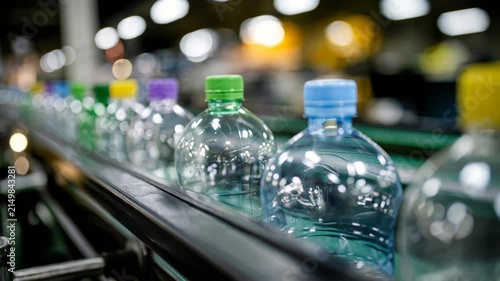 Clear plastic bottles with colorful caps move on conveyor belt in dynamic close-up factory footage.