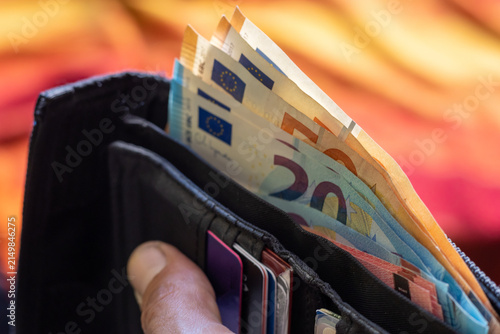 Fotografie Black wallet filled with Euro banknotes and credit cards held in hand