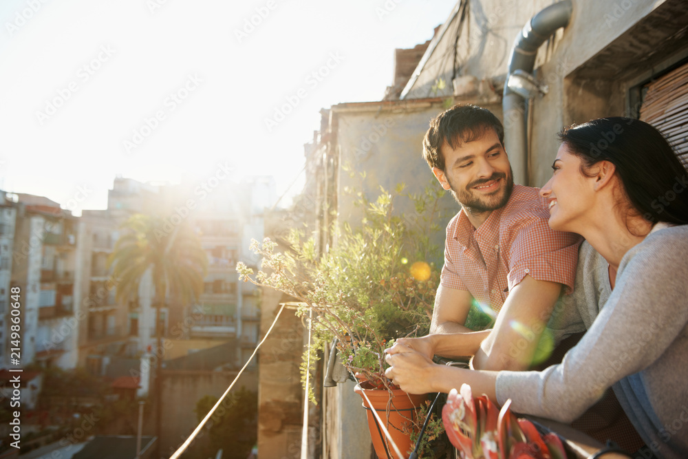 Obraz premium Happy, love and couple on balcony in morning for connection, relax and romantic moment. Dating, apartment and man with woman with sunshine for bonding, conversation and relationship on weekend