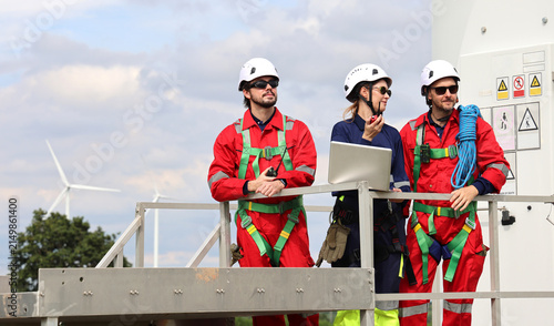 A team of professional white European male and female engineers are reviewing data on laptops and discussing maintenance at a renewable energy wind farm.
