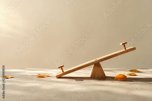 Tiny tilted wooden seesaw model with scattered autumn leaves, balance and prepared practical concept.