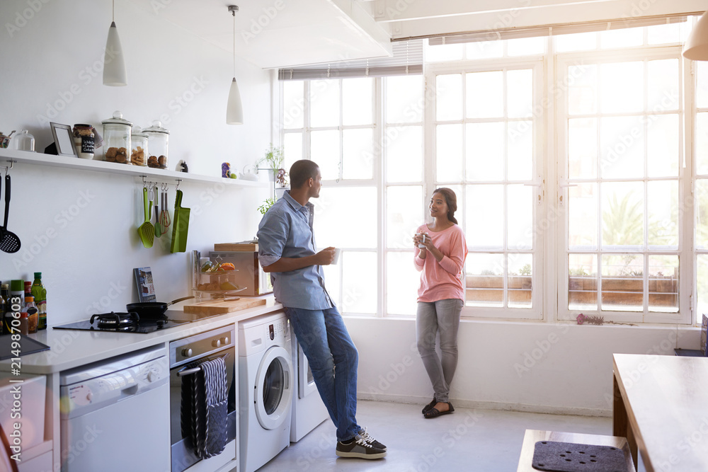 Obraz premium African couple, morning and coffee with relax in kitchen for bonding, relationship or holiday together. Home, happy man and woman with break for comfort, support and chat with conversation in house
