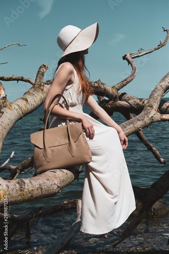woman with a handbag sitting on a tree in a hat 