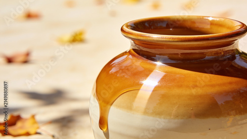 Golden honey dripping down a traditional ceramic pot in warm autumn sunlight with fallen leaves