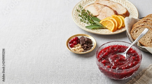 Cranberry sauce in glass bowl with roasted turkey slices and bread. Festive dinner setting for Thanksgiving celebration. Traditional holiday meal preparation on table with copy space.